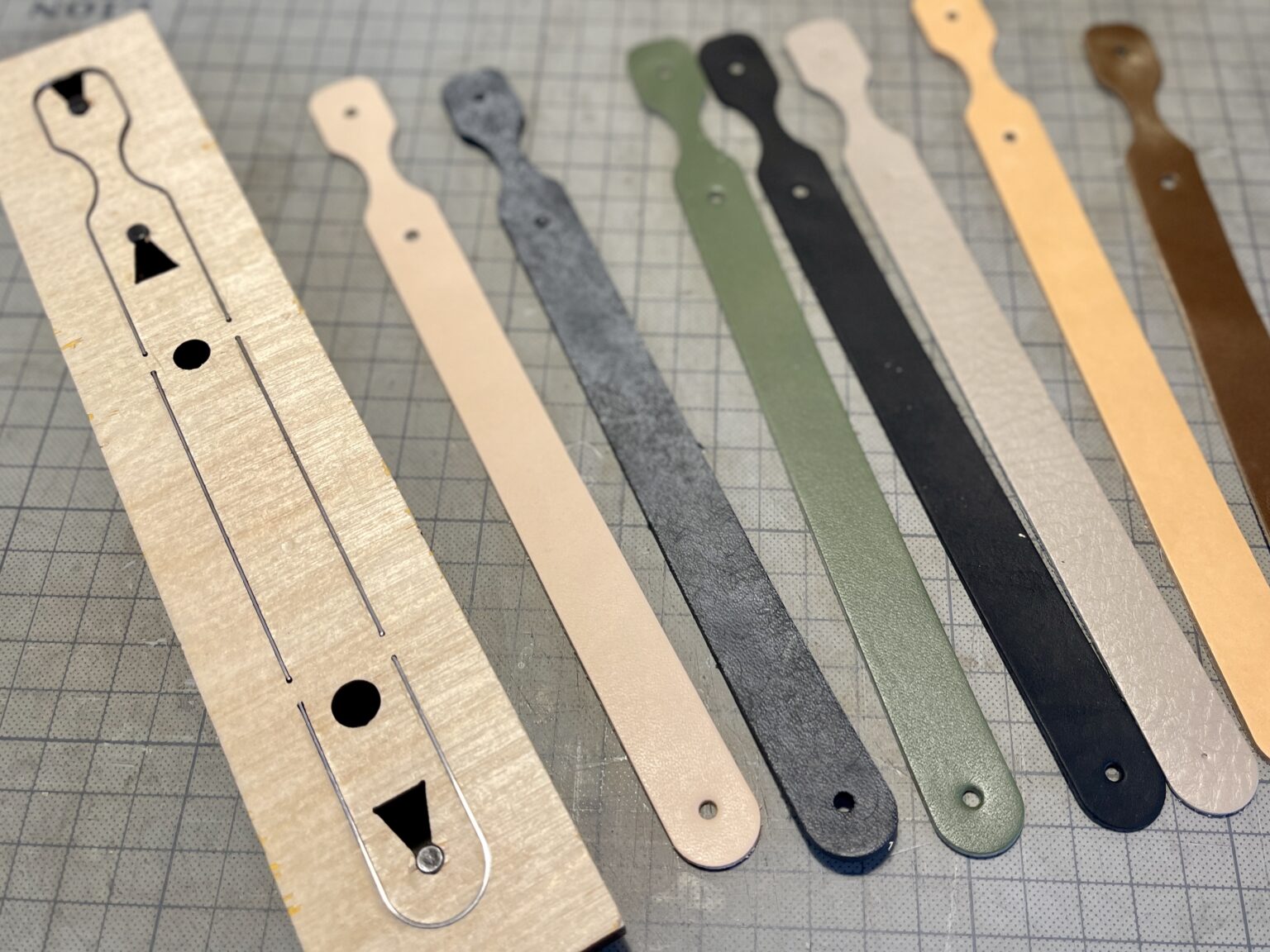 レザークラフトの抜き型でカットした7種類の異なる革（ヌメ革、シュリンクレザー等）のキーホルダーパーツが並んでいる様子。万能プレス機ALL-2000による量産検証の風景。